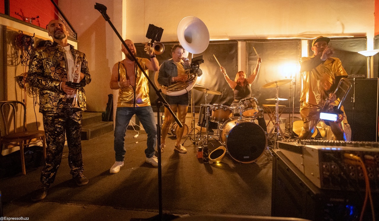Musicians dress in metallic gold on stage holding instruments but singing
